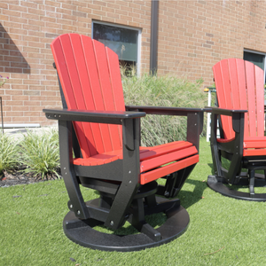 Two red and black Adirondack swivel glider chairs on a grassy area with a building in the background.