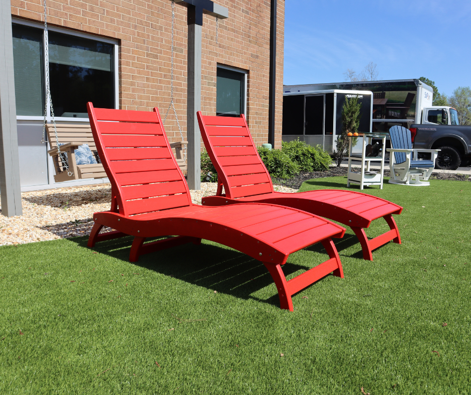 Two red curved lounge chairs on a grassy area with a building and truck in the background.