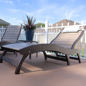 Two curved lounge chairs on a deck with a white picket fence and blue sky in the background.